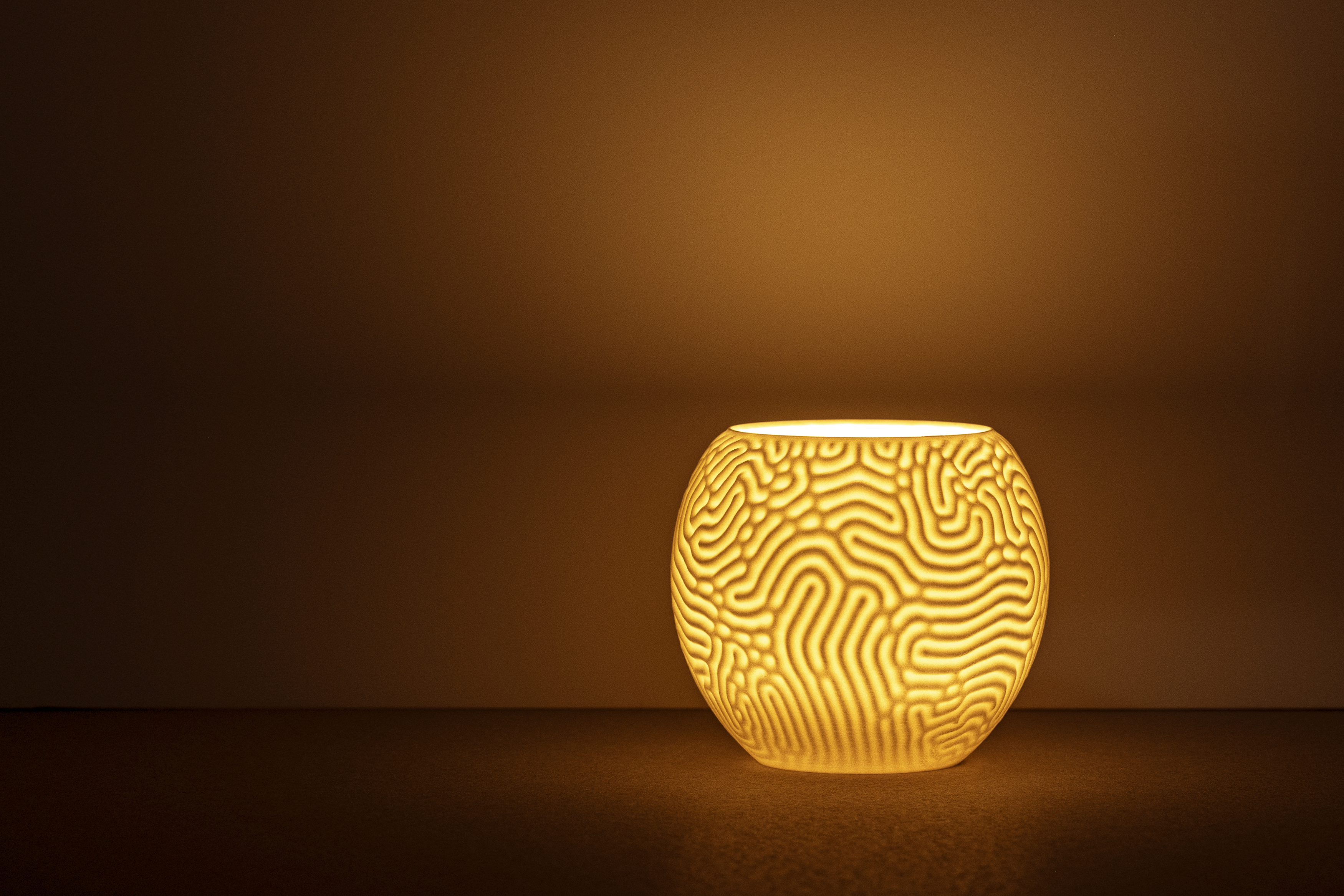 Decorative suggestion for Aeolian Plains: Tealight holder with a nature-inspired design. Evokes reveries of dune patterns - variant Original (Elegant white), an original product by Cosmic Jubilee (1 of 3) - presented as a tealight, switched on.