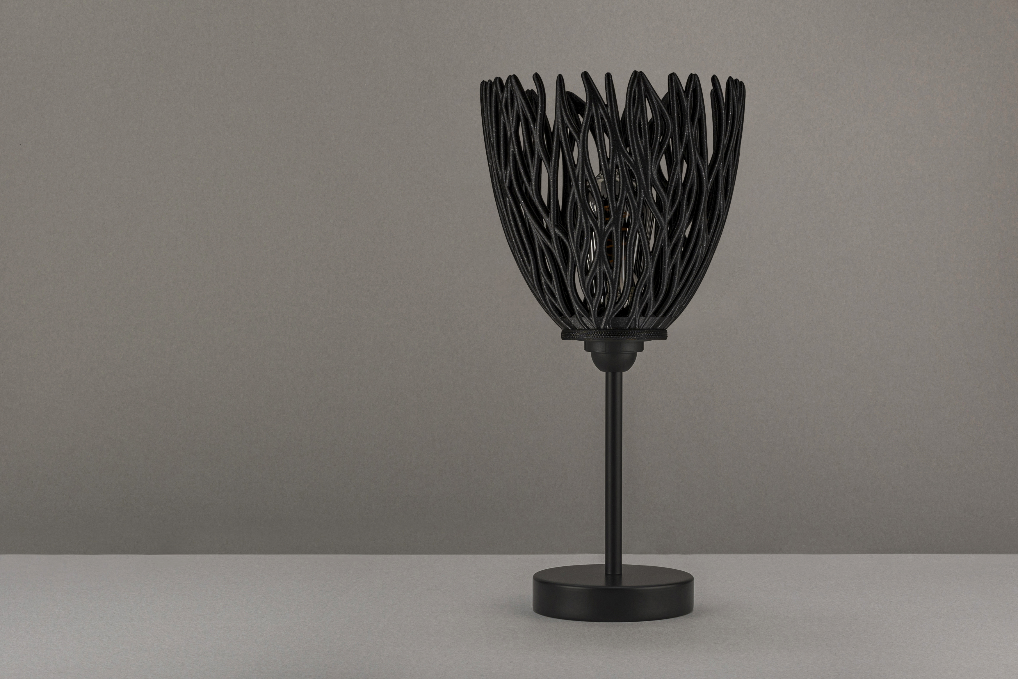 Decorative suggestion for Empyreal Bloom: Pendant lampshade with organic growth design. Mesmerizing shadow play for subtle elegance and ambiance - variant Original (Black with a hint of sparkle), an original product by Cosmic Jubilee (5 of 8) - presented as desktop, table, or freestanding light, switched off.