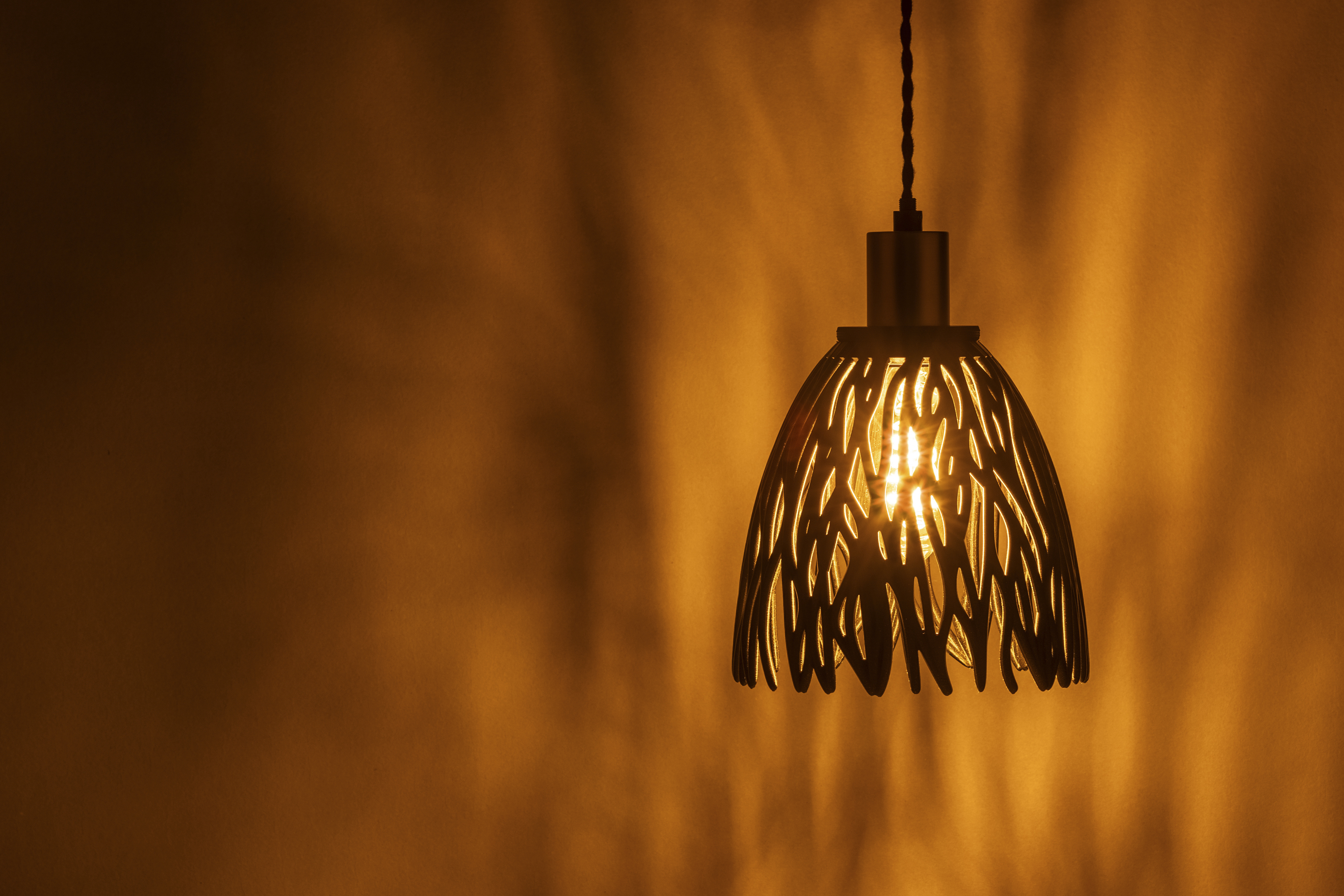 Decorative suggestion for Empyreal Bloom: Pendant lampshade with organic growth design. Mesmerizing shadow play for subtle elegance and ambiance - variant Original (Black with a hint of sparkle), an original product by Cosmic Jubilee (2 of 8) - presented as pendant light, hanging from ceiling, switched on.