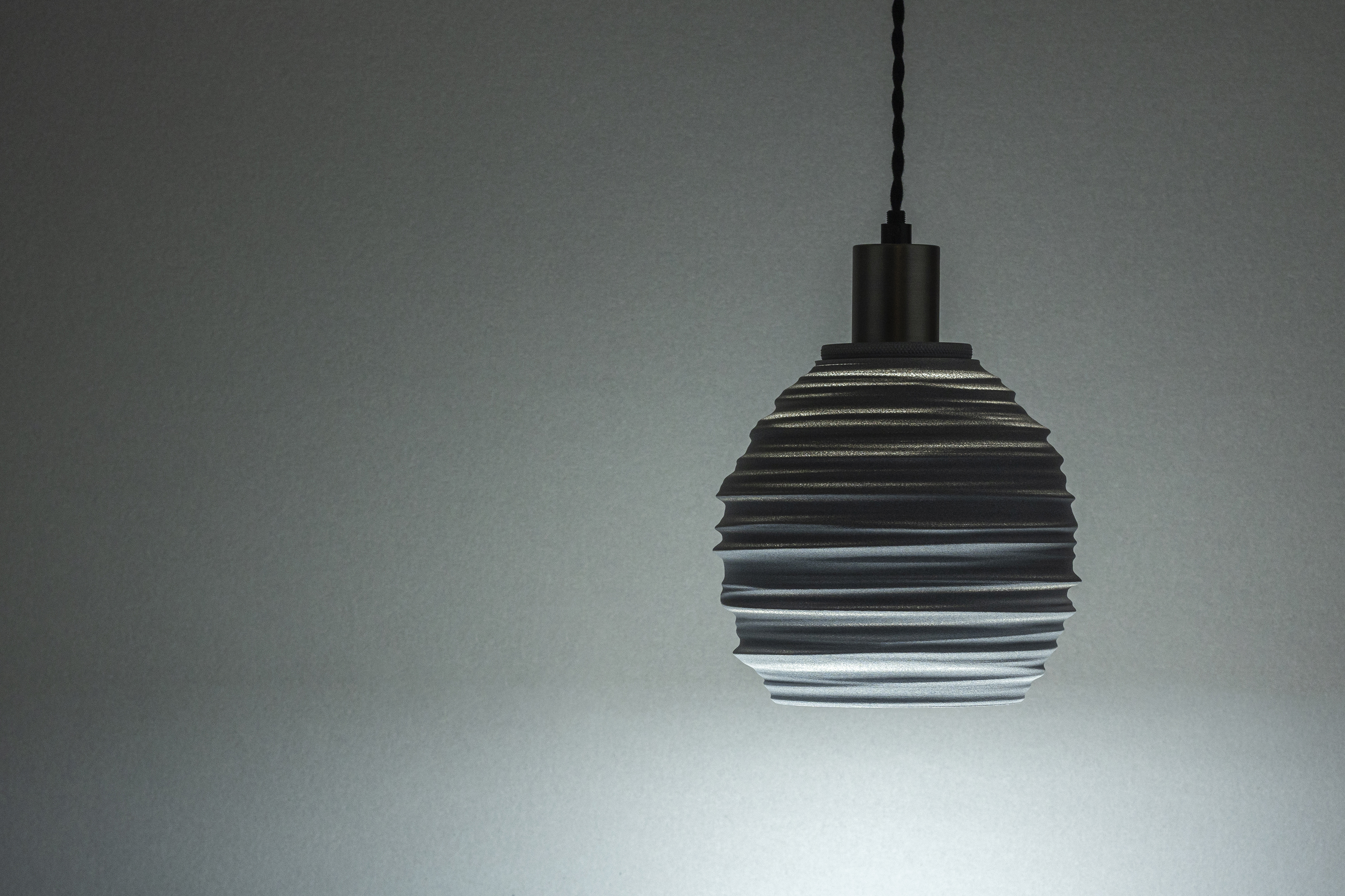 Decorative suggestion for Magma Shroud: Pendant lampshade mirroring tumultuous magma flow. Adds an elemental touch to modern decor - variant Granite Gray (Grainy textured stone gray spotlight), an original product by Cosmic Jubilee (1 of 6) - presented as pendant light, hanging from ceiling, switched on.