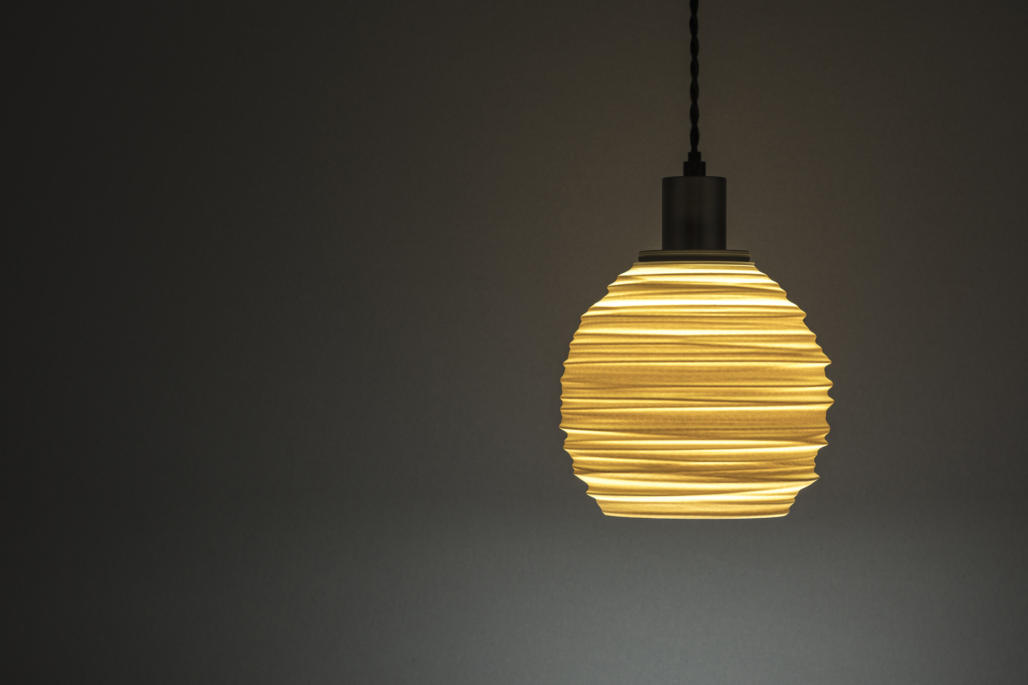 Decorative suggestion for Magma Shroud: Pendant lampshade mirroring tumultuous magma flow. Adds an elemental touch to modern decor - variant Original (Creme and beige diffuse light), an original product by Cosmic Jubilee (1 of 6) - presented as pendant light, hanging from ceiling, switched on.