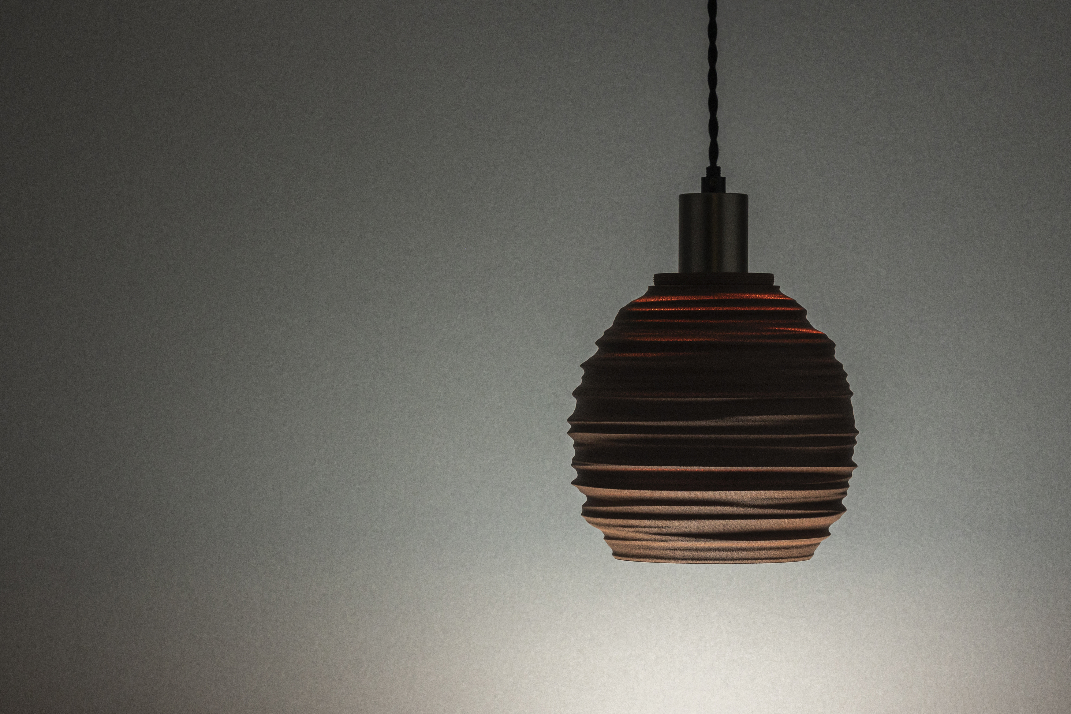Decorative suggestion for Magma Shroud: Pendant lampshade mirroring tumultuous magma flow. Adds an elemental touch to modern decor - variant Stone Red (Grainy textured stone red spotlight), an original product by Cosmic Jubilee (1 of 6) - presented as pendant light, hanging from ceiling, switched on.