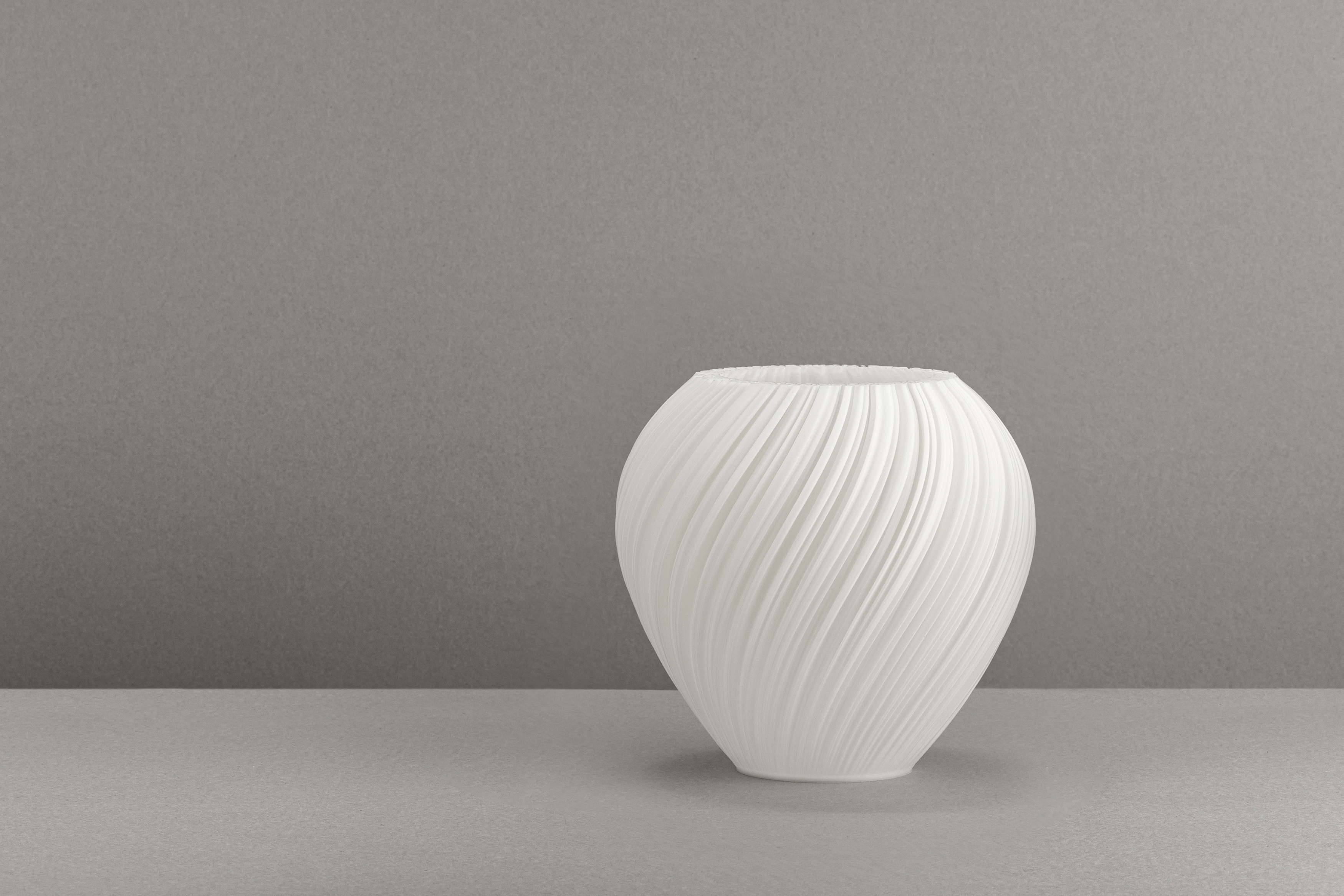 Decorative suggestion for Pellucid Sweep: Spiraling pleats pendant lampshade for a balletic light play. Transforms environments with mesmerizing beauty - variant Original (Milky white), an original product by Cosmic Jubilee (5 of 6) - presented as a decorative (non-water) vase or standalone showpiece.
