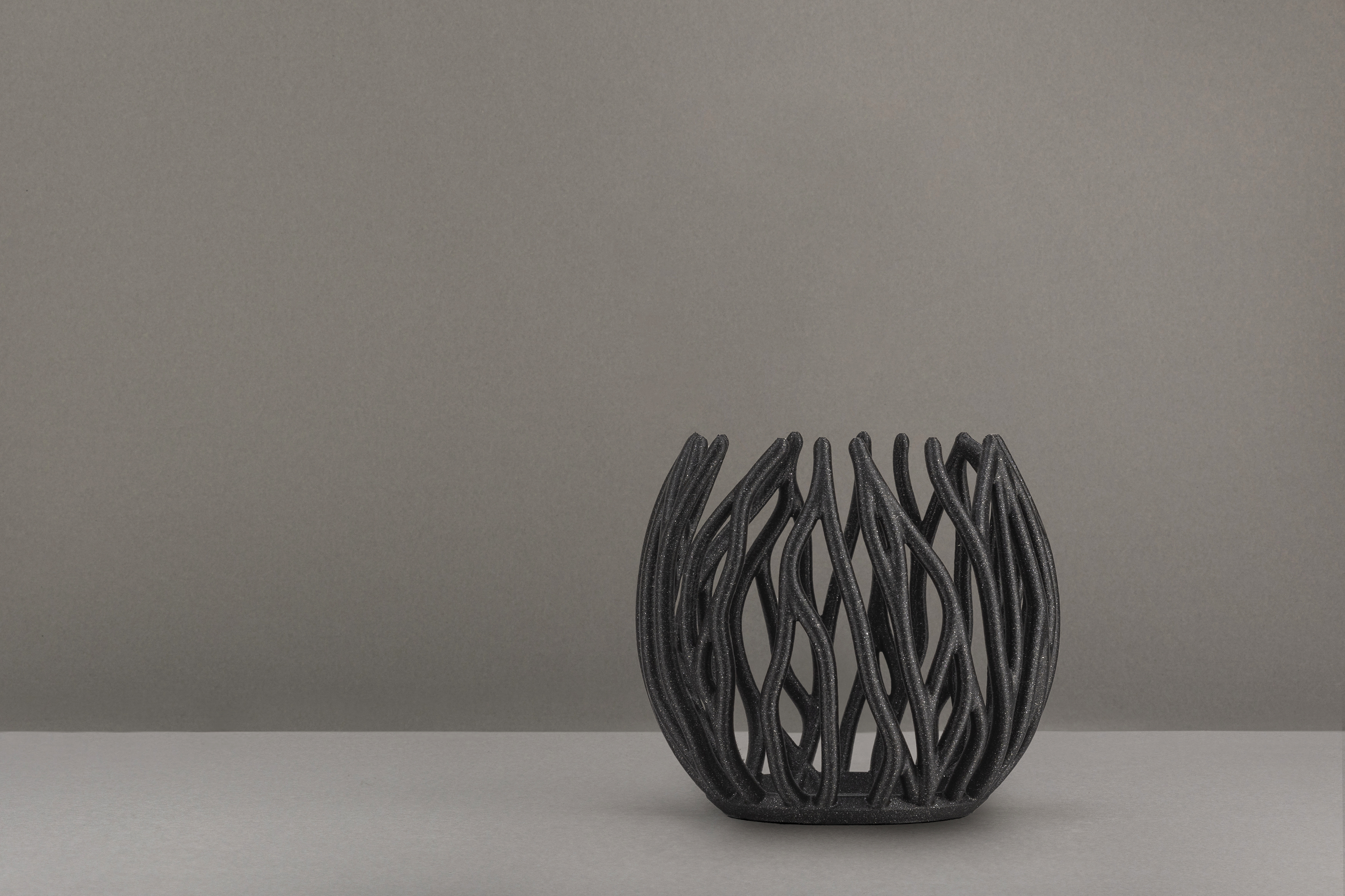 Decorative suggestion for Twinkling Bloom: Elegant tealight holder with organic, floral-inspired design. Mesmerizing shadow play for subtle elegance and ambiance - variant Original (Black with a hint of sparkle), an original product by Cosmic Jubilee (2 of 3) - presented as a tealight, switched off.